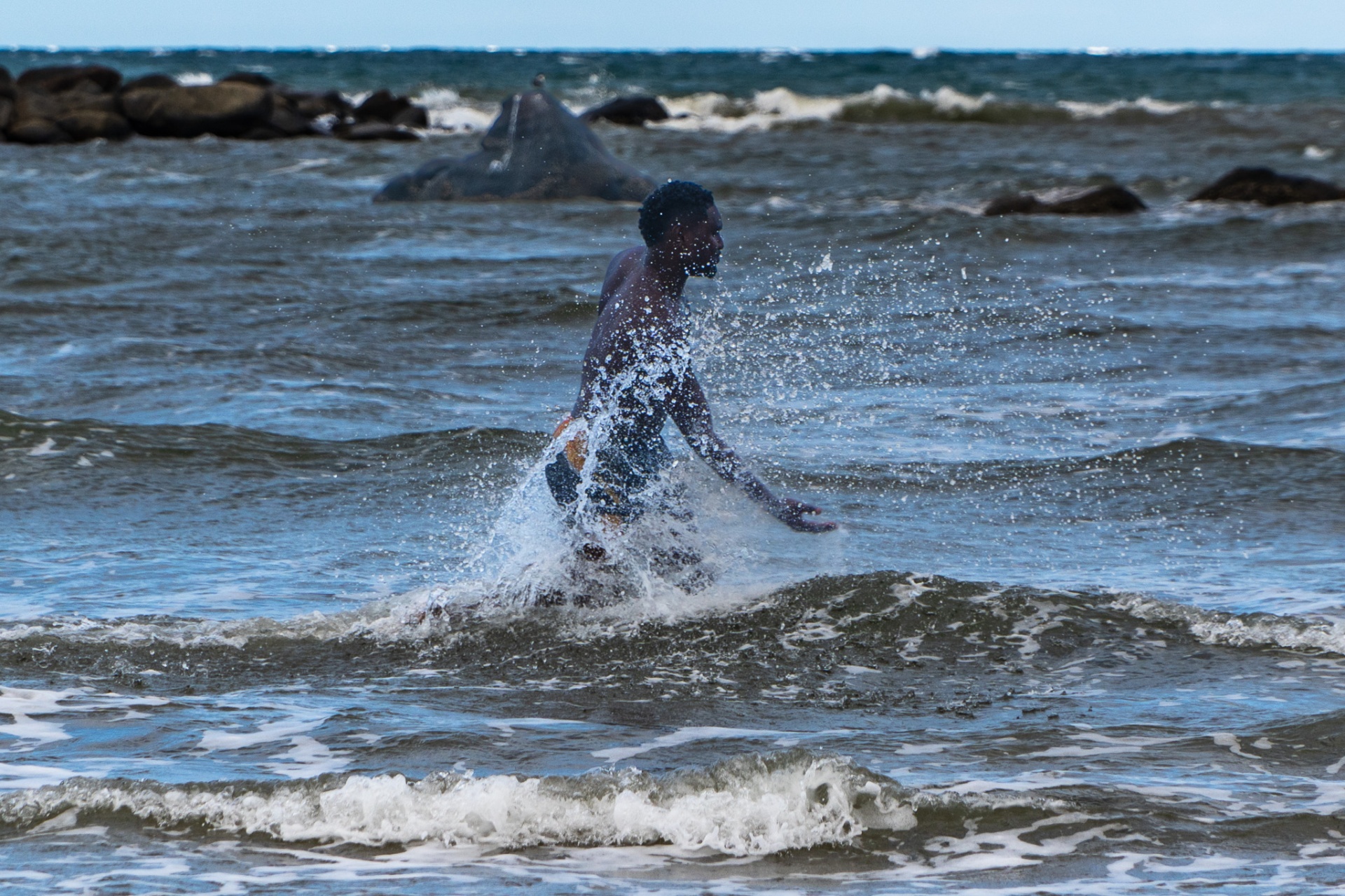 A brother running through breaking waves, water splashing wildly